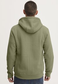 Felpa verde oliva con cappuccio regolabile, polsini e orlo a coste, realizzata in tessuto morbido. Design semplice, senza motivi o loghi visibili.