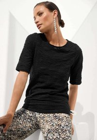 Zwarte gestructureerde top met korte mouwen en golvend ontwerp, gecombineerd met gepatternde leggings met beige, blauwe en zwarte geometrische vormen.
