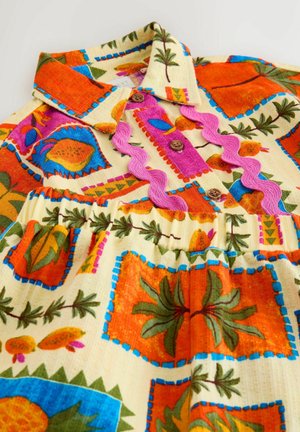 Sukienka dziecięca z wielokolorowymi wzorami owoców i liści, drewniane guziki, różowy ozdobny zygzakowy brzeg oraz elastyczna talia na jasnym tle materiału.