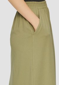 Groene, elastische taillebandrok met zijzakken, met een gladde textuur en een eenvoudig ontwerp. De stof lijkt licht en vloeiend.