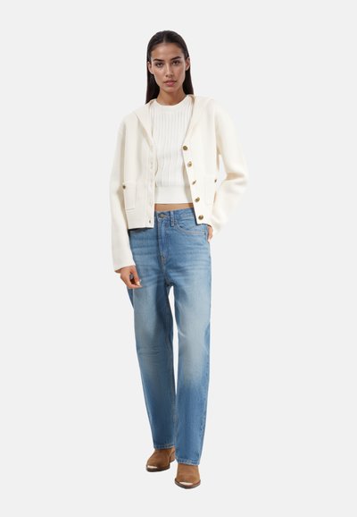 Hvid cropped cardigan med guldknapper, parret med lyseblå straight-leg jeans. Glat stofstruktur og afslappet pasform.