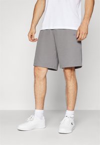 Shorts de mezcla de algodón grises con cintura elástica, bolsillos laterales y logo bordado en el muslo izquierdo, combinados con zapatillas blancas.