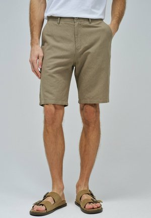 Bermudas de algodón beige con un ajuste ceñido, cierre de botón y dobladillos vueltos, combinadas con sandalias marrones con una tira ancha y una hebilla decorativa.