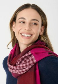 Wollen sjaal van een mengsel met een pied-de-poule en effen patronen in tinten fuchsia en bordeaux, losjes om de nek gedrapeerd.