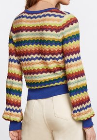 Multikleurige cardigan met zigzagpatronen in schaduw van rood, blauw, groen en goud. Brei-textuur met geribbelde blauwe manchetten en boord.