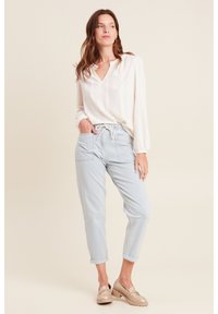 Witte blouse met lange mouwen en gatenpatroon; lichtblauwe joggerbroek met opgerolde manchetten en een trekkoord; beige instappers.