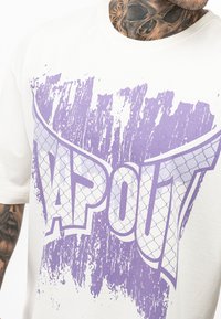 Hvid bomulds t-shirt med et stort lilla "TAPOUT" grafik med et slidt udseende og meshmønsterdetaljer. Korte ærmer, afslappet pasform.