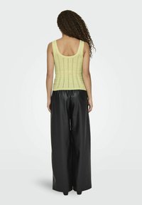 Geel, gebreide tanktop met een ronde rug, gecombineerd met zwarte, wijde, glanzende pantalons. De top heeft verticale strepen voor textuur.