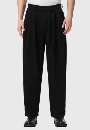 Schwarze, locker sitzende Hose mit vorderen Falten, elastischen Bündchen und Seitentaschen, kombiniert mit schwarzen Lederstiefeln und einem weißen Oberteil.