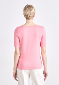 Roze top met korte mouwen, zachte textuur, ronde halslijn en opgerolde mouwmanchetten, gecombineerd met lichtgekleurde broeken.