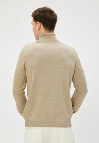 Beige Rollkragenpullover mit geripptem Kragen und Bündchen. Weiche Textur und taillierter Schnitt, mit nahtlosem Rücken und ohne sichtbare Beschläge.
