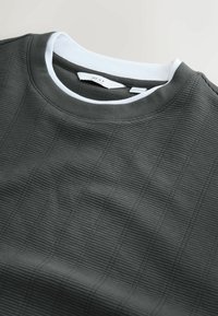 Mørkegrå sweatshirt med tekstur, der har ribbet stof med tynde lodrette striber og en hvid crew-neck. Etiketten er synlig inden i kraven.