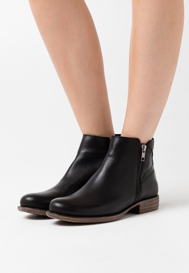 Botas de cuero negro hasta el tobillo con punta redondeada, cremallera lateral y tacón apilado. Textura suave y diseño minimalista.