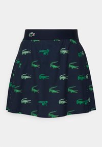 Marinblå skorts med ett grönt krokodilmönster och Lacoste-logotyp; har en elastisk midja och en plisserad design för enkel rörelse.