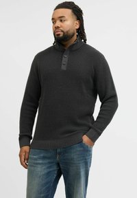 Dark gray textured sweater with a high collar, featuring three buttons and ribbed cuffs and hem, paired with faded blue jeans.