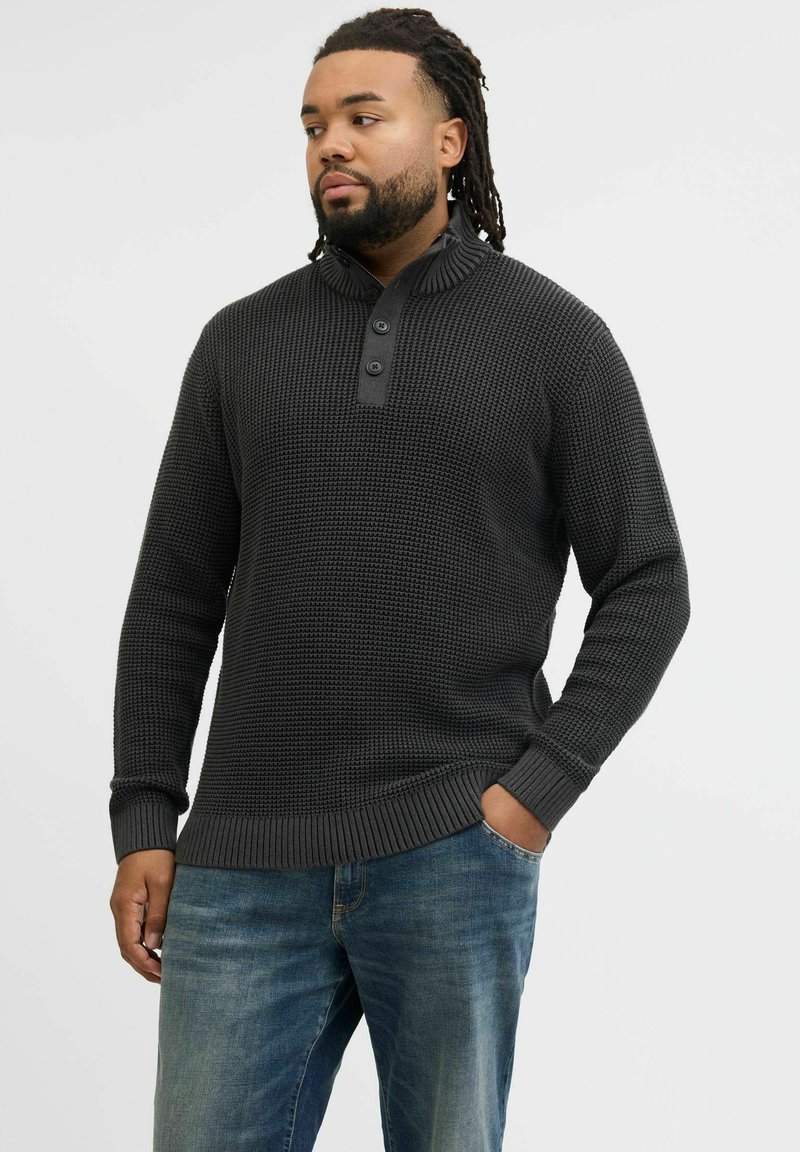 Dark gray textured sweater with a high collar, featuring three buttons and ribbed cuffs and hem, paired with faded blue jeans.