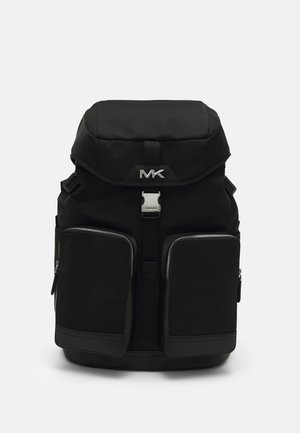 Sac à dos noir avec rabat supérieur, boucle métallique à l'avant, deux grandes poches zippées à l'avant et logo MK sur le rabat sur fond blanc.