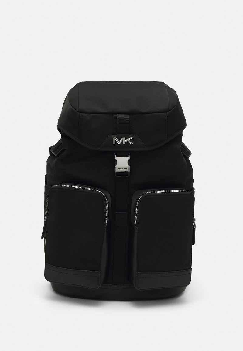 Sac à dos noir avec rabat supérieur, boucle métallique à l'avant, deux grandes poches zippées à l'avant et logo MK sur le rabat sur fond blanc.
