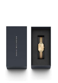 Montre avec bracelet en mailles dorées et un cadran rectangulaire, présentée dans une boîte bleue foncée avec un revêtement intérieur noir. Logo gravé sur la boîte.