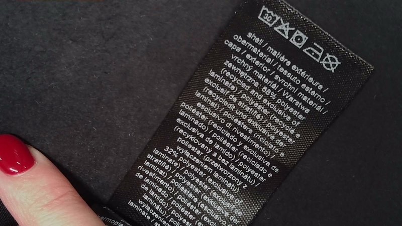 Czarna metka dotycząca pielęgnacji materiału z białym tekstem pokazuje instrukcje prania. Materiał składa się w 68% z recyklingowanego poliestru, w 32% z poliestru i zawiera symbole.