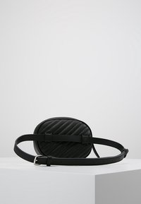 Sac bandoulière en cuir noir de forme ovale, avec un motif matelassé et une sangle réglable. Doté d'une boucle argentée pour la fermeture.