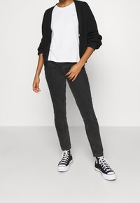 Casual outfit featuring a black knitted cardigan, white t-shirt, dark jeans, and black high-top sneakers with white soles.