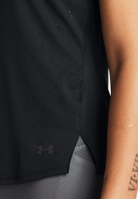Top atlético negro sin mangas con pequeñas perforaciones a los lados, con el logo de Under Armour encima de una abertura lateral, combinado con leggings grises.