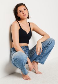 Bralette negra con un escote en V profundo, correas anchas y un diseño elegante. Combinado con jeans de cintura alta de color azul desgastado. Textura de fondo suave.