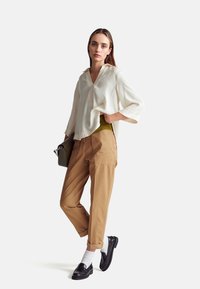 Krémová, lehká blůza s výstřihem do V a volnými rukávy; spárována s úzkými béžovými kalhotami a černými mokasíny přes bílé ponožky.