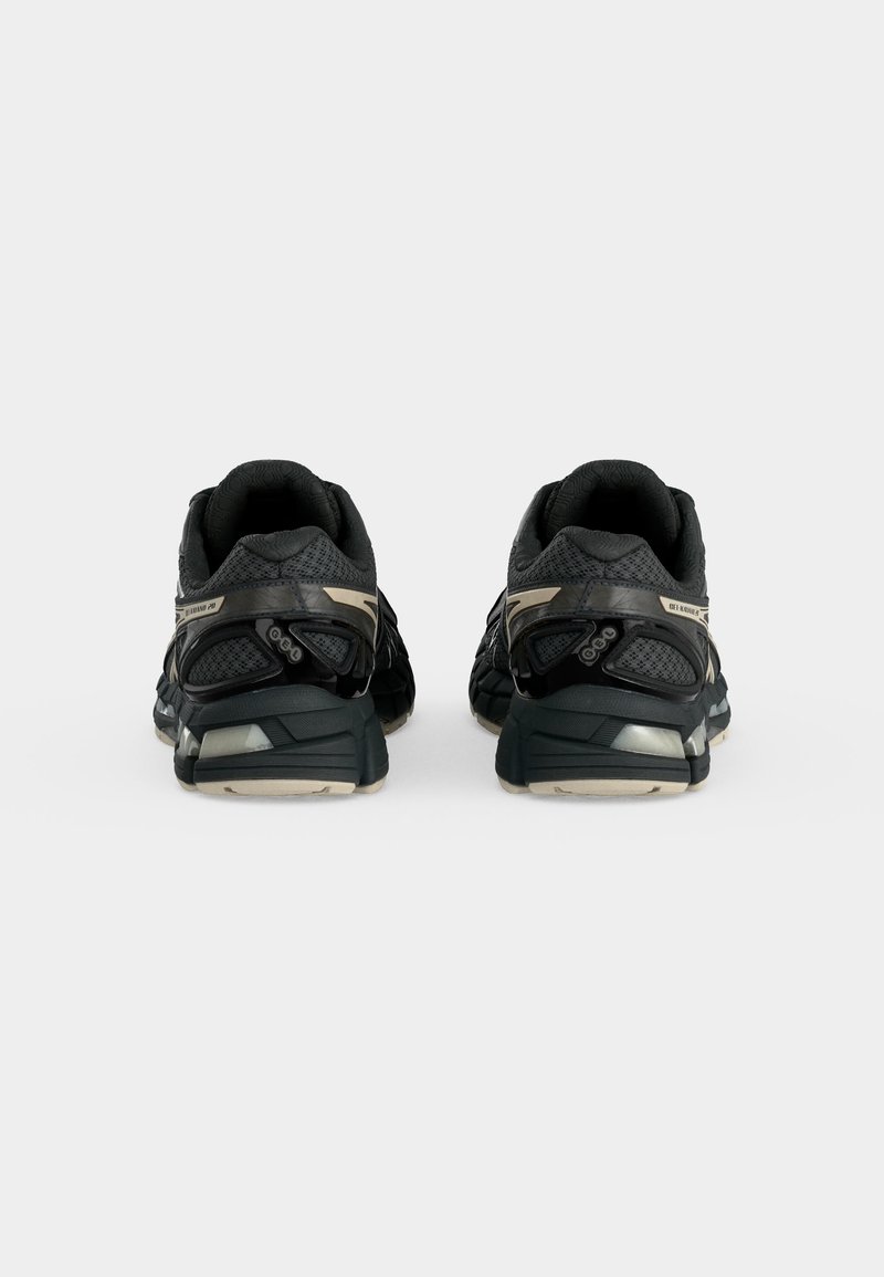Par de zapatillas deportivas negras y grises vistas desde atrás sobre un fondo blanco liso, mostrando detalles del talón y la suela.