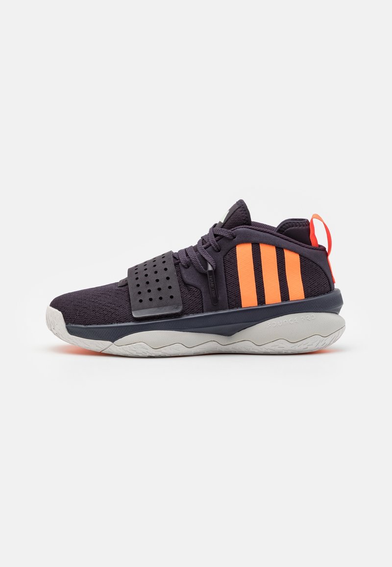 Chaussure de sport noire avec des bandes orange, une sangle perforée et une semelle blanche texturée vue de côté sur fond blanc.