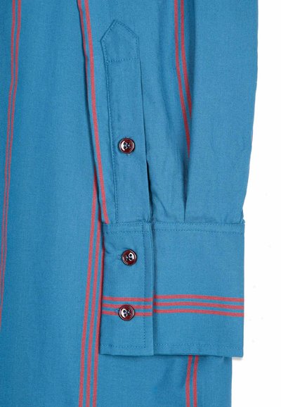 Poignet de chemise bleu à manches longues avec des rayures rouges verticales et horizontales et trois boutons rouge foncé sur le poignet et la patte de manche.