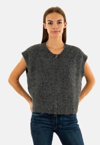Maglione cropped grigio in wool con maniche corte, finitura testurizzata e chiusura con zip frontale. Abbinato a jeans blu scuro.
