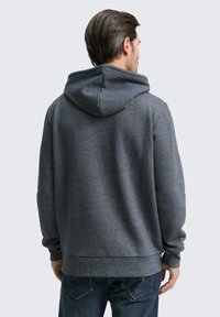 Donkergrijze fleece hoodie met een ruime kap, geribde manchetten en zoom. Heeft een zachte textuur en een ontspannen pasvorm, weergegeven van achteren.