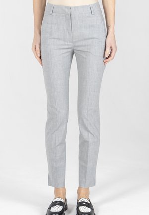 Obcisłe jasnoszare spodnie wizytowe noszone przez osobę, zestawione z czarno-białymi mokasynami, stojącą na jednolitym tle.