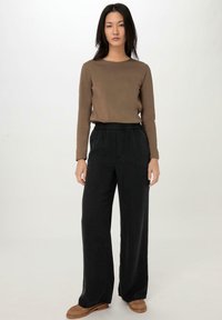 Bruine lange mouwtop met een ronde hals, gecombineerd met losse zwarte broek met een elastieken tailleband. Bruine instappers maken de outfit compleet.