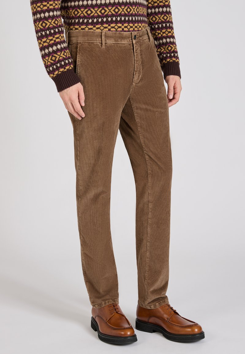 Brązowe spodnie kordurowe z pionowym prążkowaniem, pięciopunktowym designem i prostym krojem nogawki. Połączone z brązowymi skórzanymi butami na sznurówki.