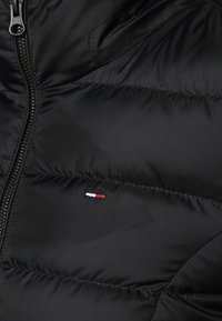 Black puffer jacket featuring a zip closure, quilted texture, and a small embroidered logo in red, white, and blue on the left side.