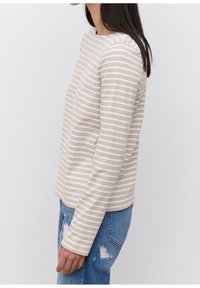 Beżowa bluzka z długim rękawem w białe poziome paski, okrągły dekolt i luźny krój. Połączona z jasnoniebieskimi zniszczonymi dżinsami.