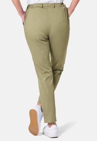 Hellgrüne Hosen mit tapered Design, elastischem Bund, Seitentaschen und glatter Textur, kombiniert mit weißen Sneakern.