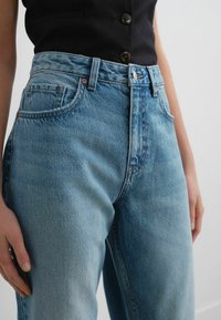 Jeans de denim azul claro con cintura alta, que cuentan con bolsillos frontales, costuras visibles y un ajuste relajado. El material parece suave y desgastado.