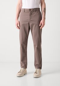 Bruine katoenen broek met een rechte snit, voorzien van een ritssluiting en knoopsluiting, twee voorkruiszakken en een zachte textuur. Gecombineerd met beige sneakers.