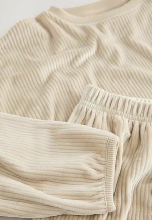 Beige ribbad kangas komplekt, mis sisaldab pikkade varrukatega toppi ja elastse vöökohtaga pükse. Pehme tekstuur, millel on peened vertikaalsed read ja viimistletud õmblused.