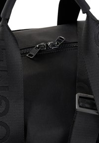 Svart nylonväska med dubbel dragkedjestängning, strukturerade remmar och diskret branding. Slät yta med matta detaljer och en stilren design.