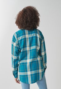 Camicia a scacchi turchese con maniche lunghe, caratterizzata da un motivo a quadri con accenti blu chiaro, verde e giallo. Tessuto morbido, vestibilità comoda.
