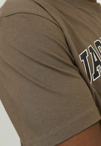 Løs pasform, kortærmet t-shirt i muted brun bomuld med glat tekstur; har trykt tekst i kontrastfarve over brystområdet.