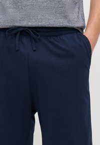 Navy siniset jogger-housut, jotka on valmistettu pehmeästä puuvillasta. Niissä on joustava vyötärö, nyörisulku ja sivutaskut; sileä pinta.