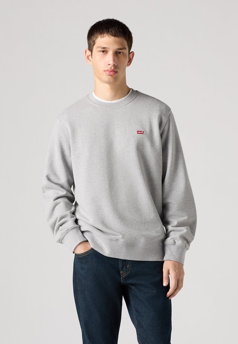 Gray sweatshirt with ribbed cuffs and hem, featuring a small red Levi's logo on the chest. Paired with dark blue jeans.