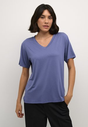 T-shirt violette à col en V en tissu doux, avec des manches courtes et une coupe décontractée, associée à un pantalon noir. Texture lisse, design simple.