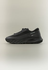 Μαύρο αθλητικό παπούτσι με υφή στο επάνω μέρος, ελαφρύ σχεδιασμό και παχιά λαστιχένια σόλα. Διαθέτει κορδόνια και λογότυπο της μάρκας στο πλάι.
